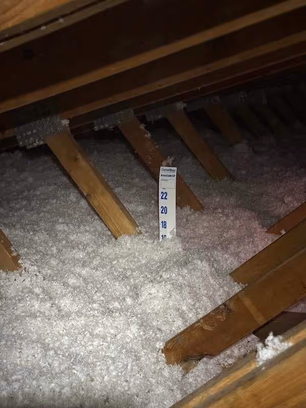 Measuring stick in loose insulation between wooden attic floor joists
