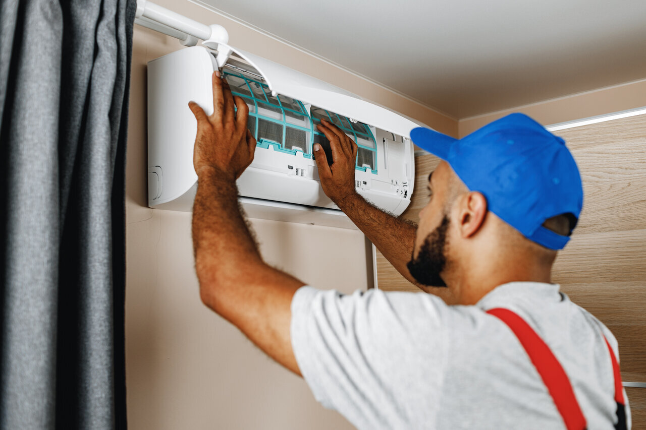 Technician in blue cap repairing air conditioning unit on wall