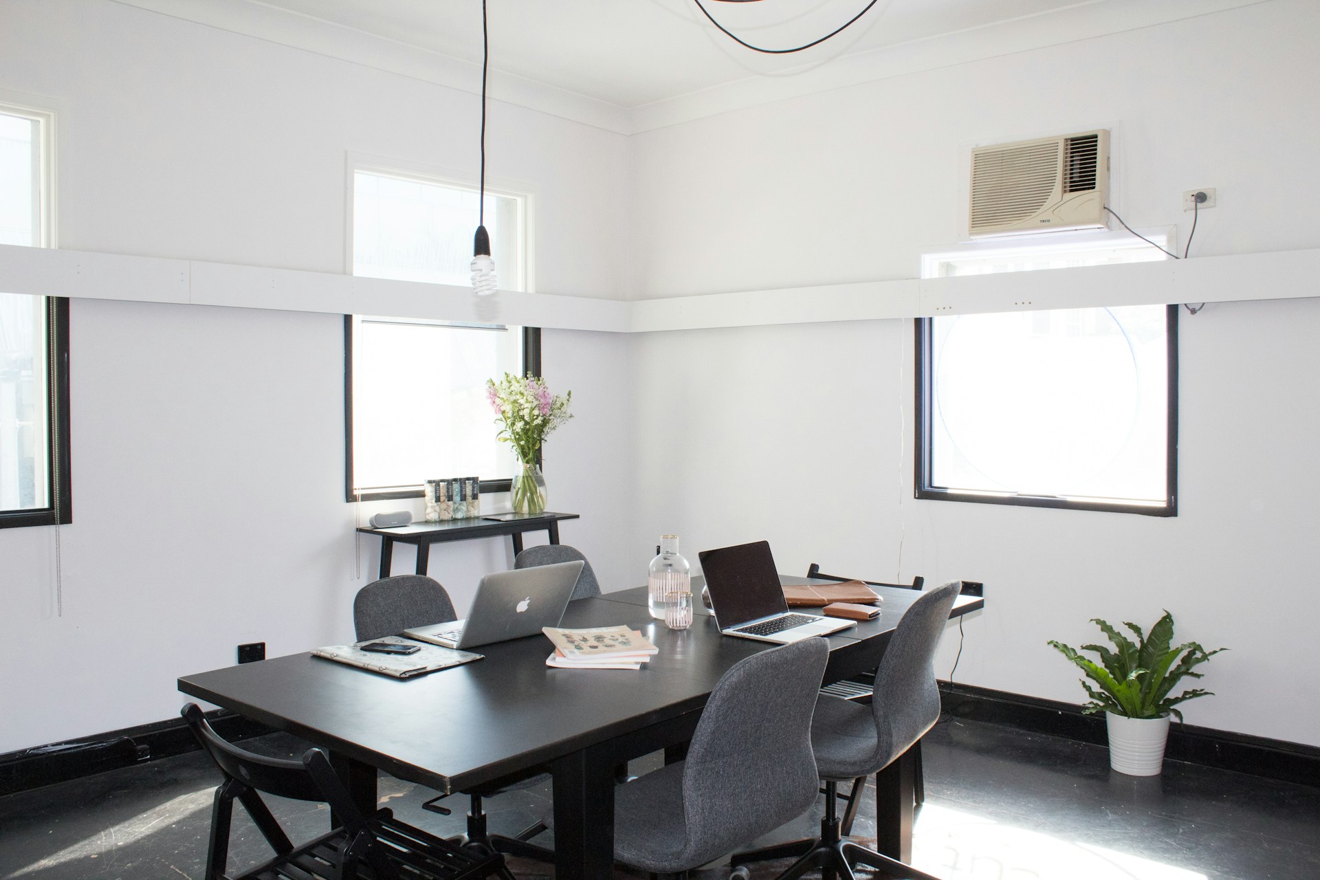 Modern home office with black table, laptops, and plants by windows