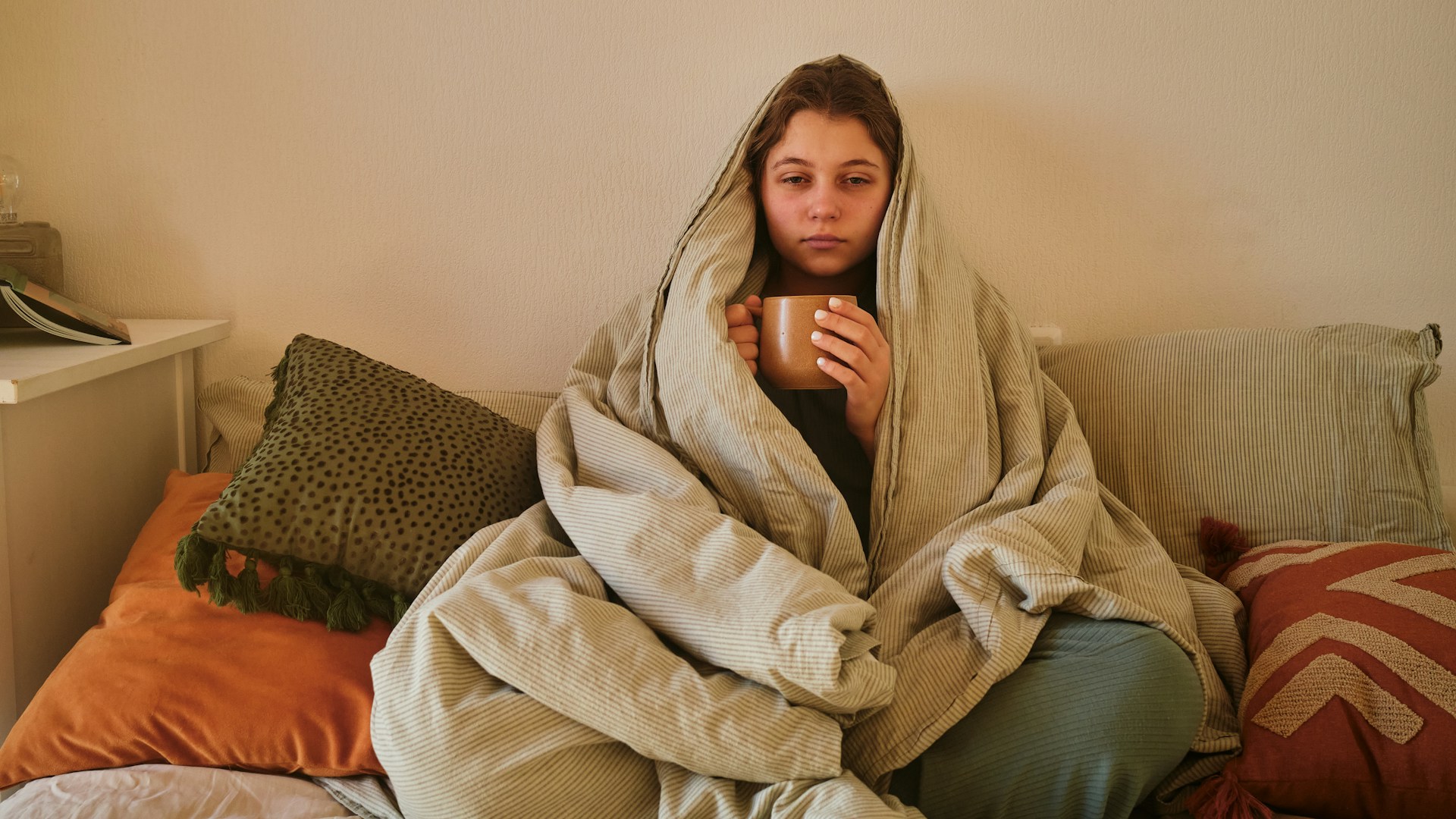 Person wrapped in blanket holding warm mug on cozy couch