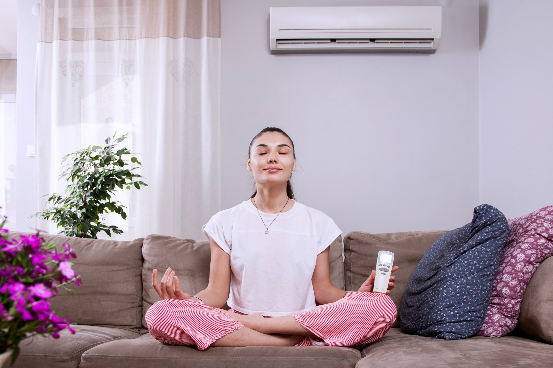 Person meditating on couch with air conditioner, plants, and remote control