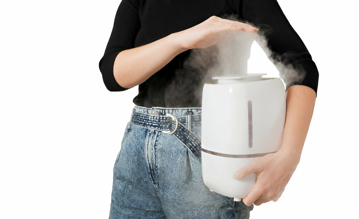 White humidifier emitting steam, held by person in black top and jeans