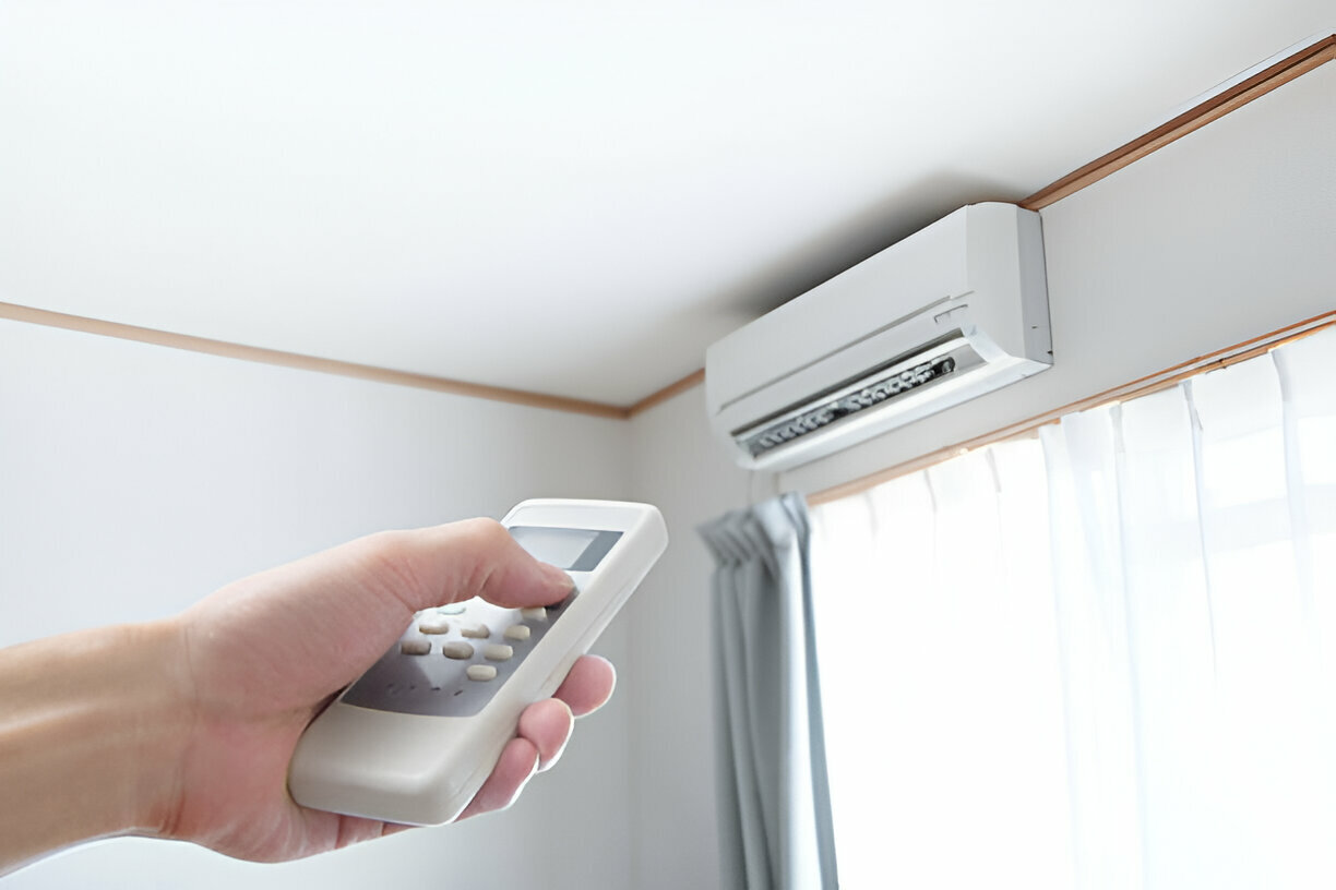 Hand holding remote control aimed at wall-mounted air conditioning unit