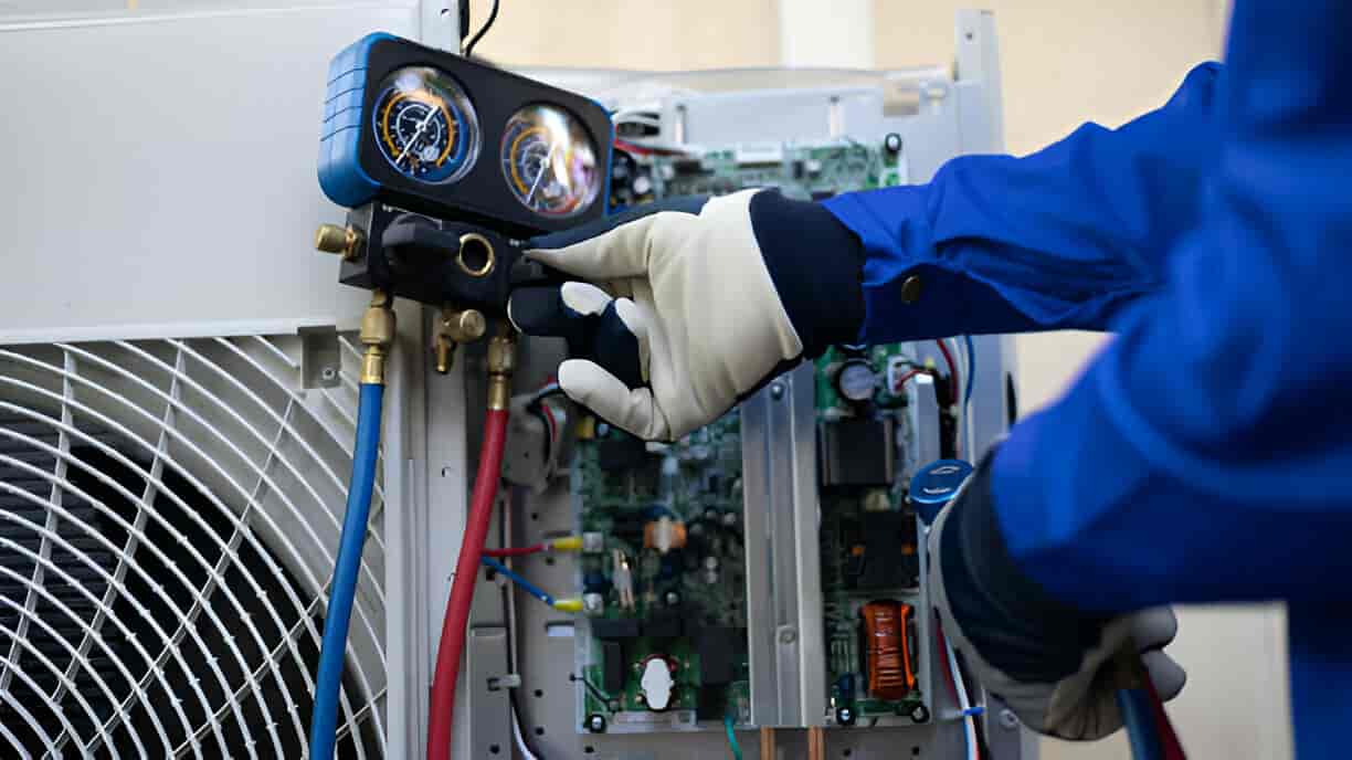 Technician checking pressure gauges on air conditioning unit's internal components