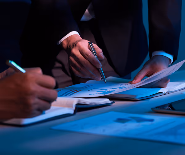 Hands filling out documents on blue-lit desk with pen