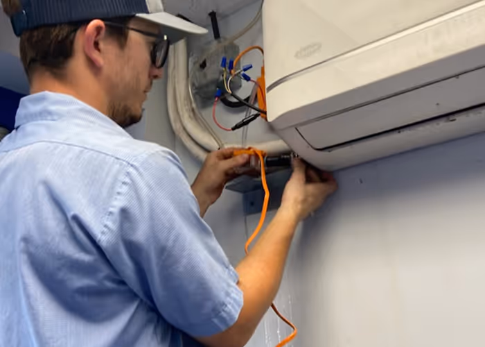 Technician installing or repairing an air conditioning unit with orange wiring