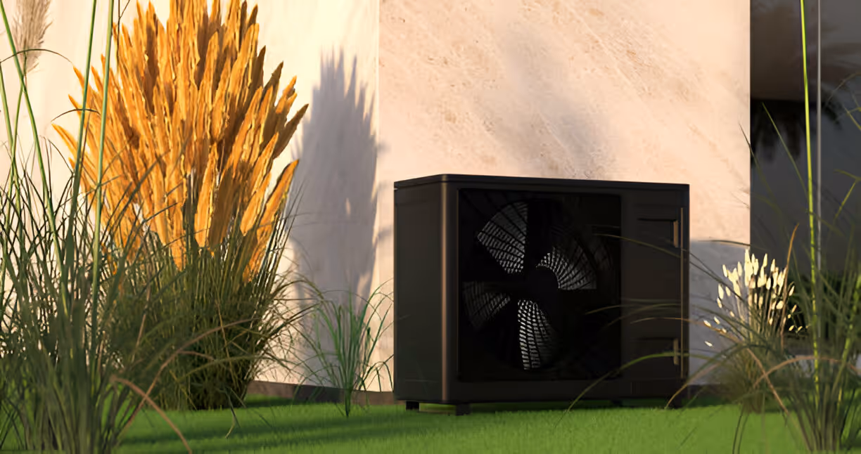 Black heat pump unit sits on green grass near ornamental wheat-colored grasses