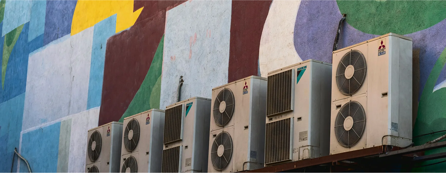 Air conditioning units mounted on colorful geometric wall background