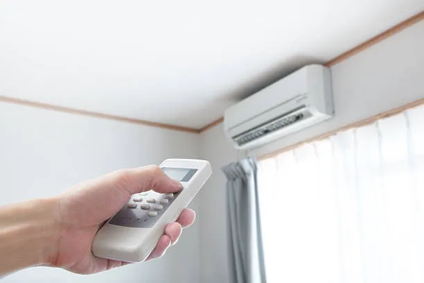Hand holding remote control adjusting wall-mounted air conditioning unit