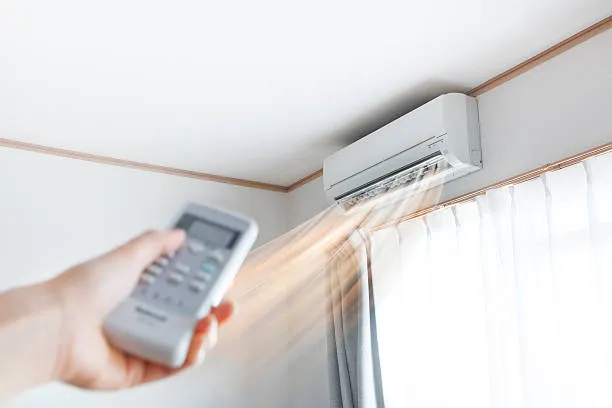 Hand using remote control to operate wall-mounted air conditioning unit