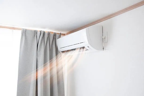 Wall-mounted air conditioner blowing cool air near gray curtains