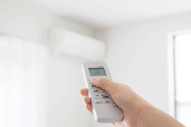 Hand holding remote control for air conditioner near wall unit