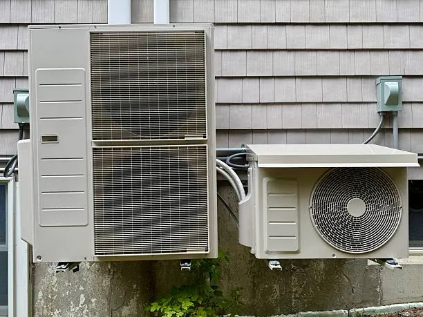 Two exterior HVAC units mounted on concrete wall with siding background