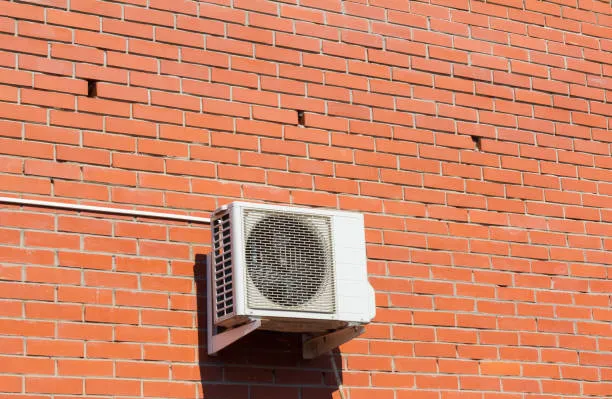 White air conditioning unit mounted on orange brick wall