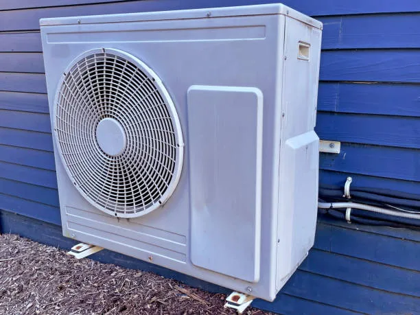 White air conditioning unit mounted on blue siding near mulched ground