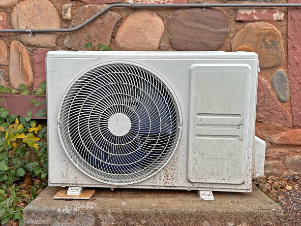 Outdoor air conditioning unit mounted on stone wall with plants nearby
