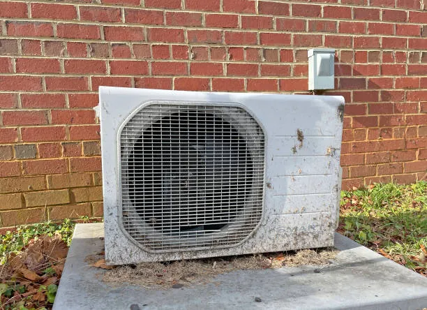 Weathered air conditioning unit mounted on concrete pad against red brick wall