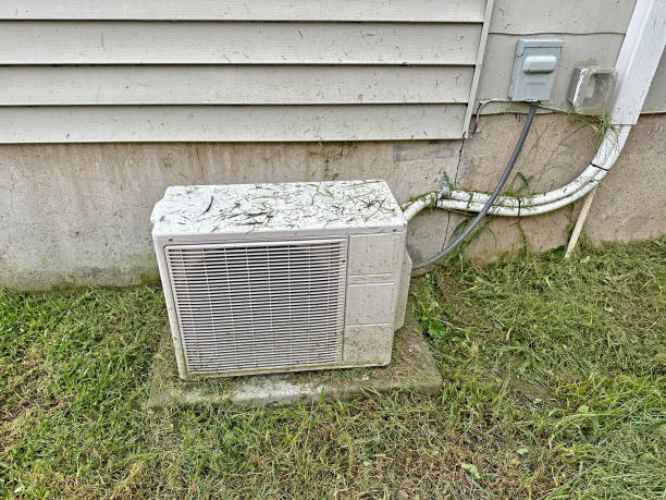 Old air conditioning unit sitting on concrete near grassy lawn and house siding