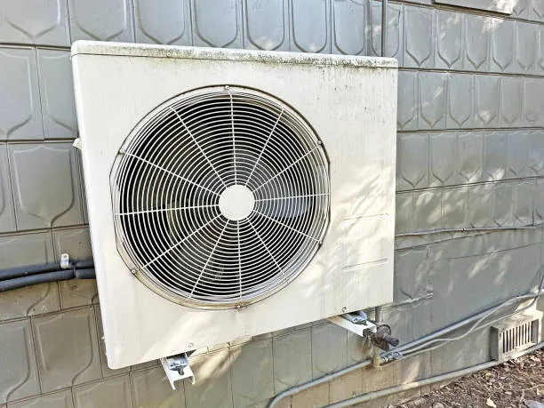 Outdoor air conditioning unit mounted on tiled wall with metal pipes