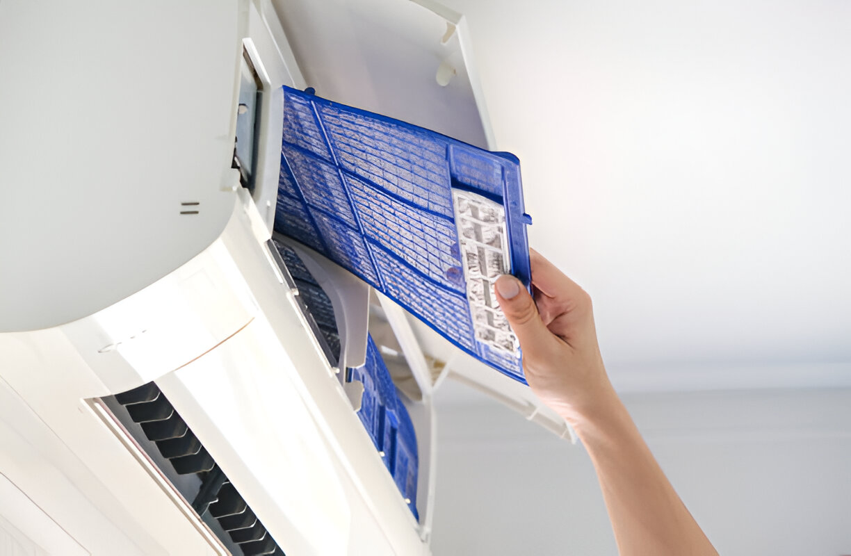 Hand removing blue air filter from white air conditioning unit
