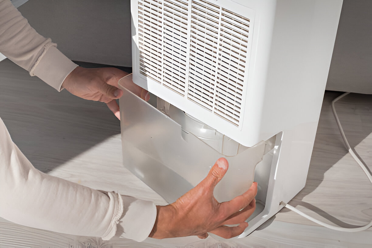 Hands adjusting water container on a white dehumidifier