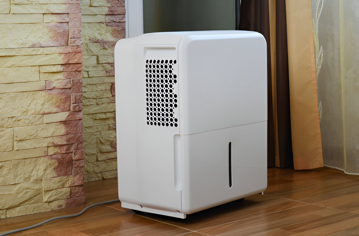 White dehumidifier placed on wooden floor near textured stone wall