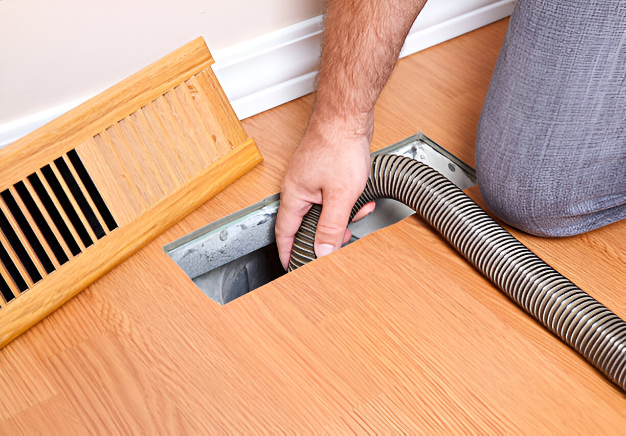 Hand checking air vent with flexible hose on wooden floor