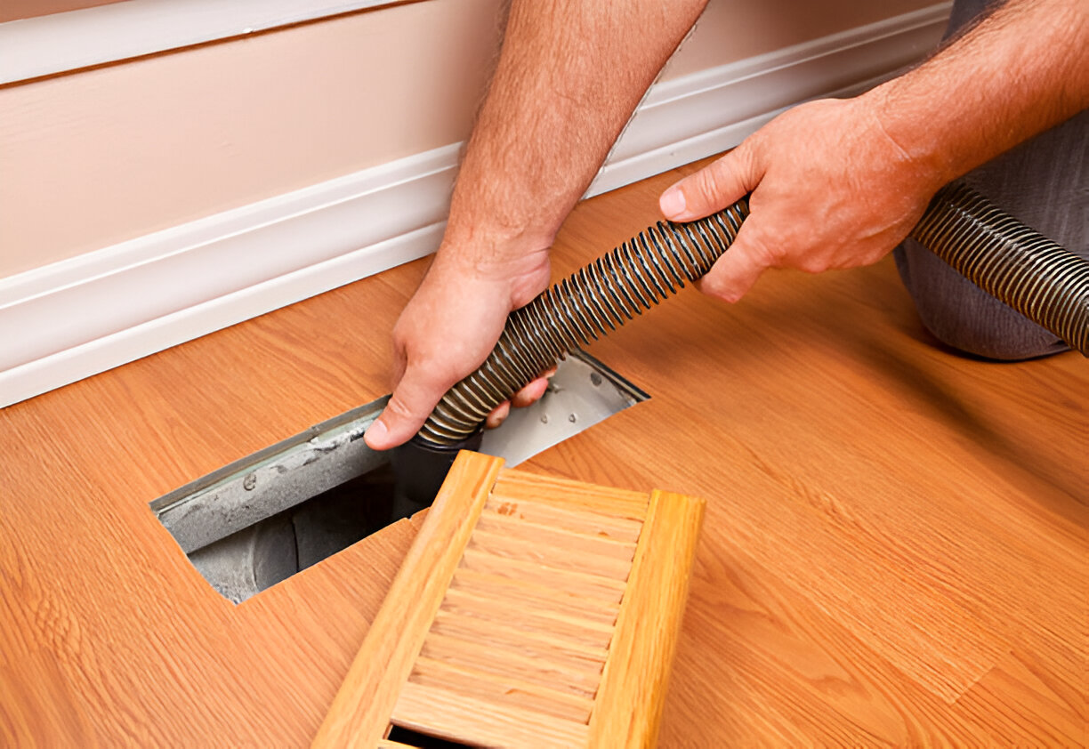 Hands connecting flexible duct to floor vent on hardwood flooring