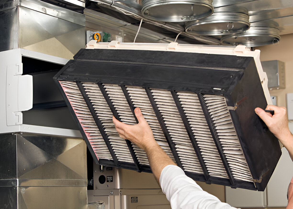 Hands removing air filter from ventilation system in commercial kitchen