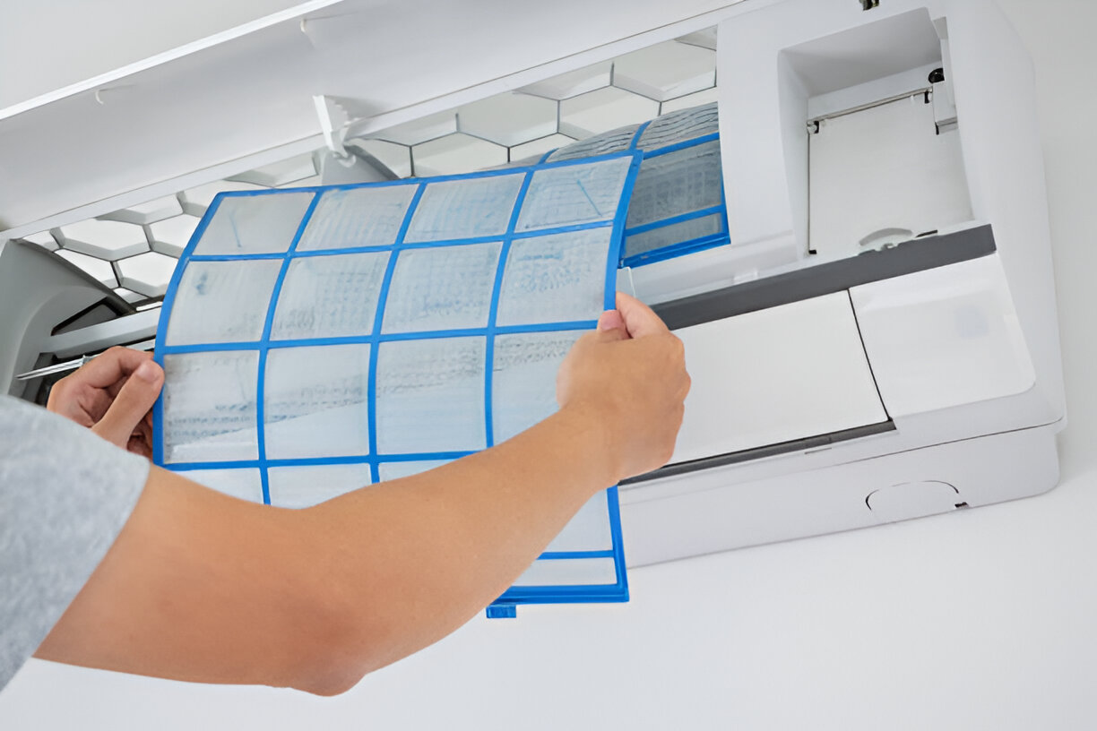 Hands removing blue-gridded filter from white air conditioning unit
