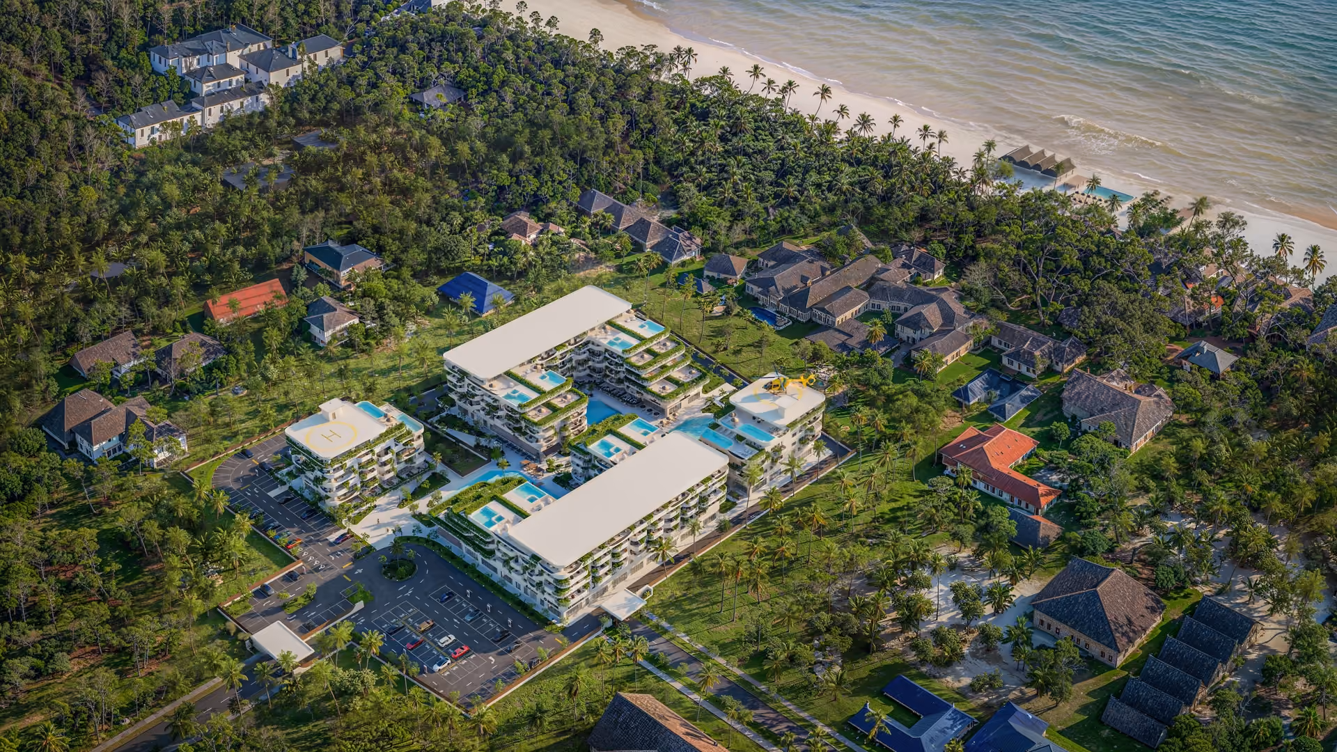 Aerial view of a modern resort with pools, helipads, and villas near a tropical beach.