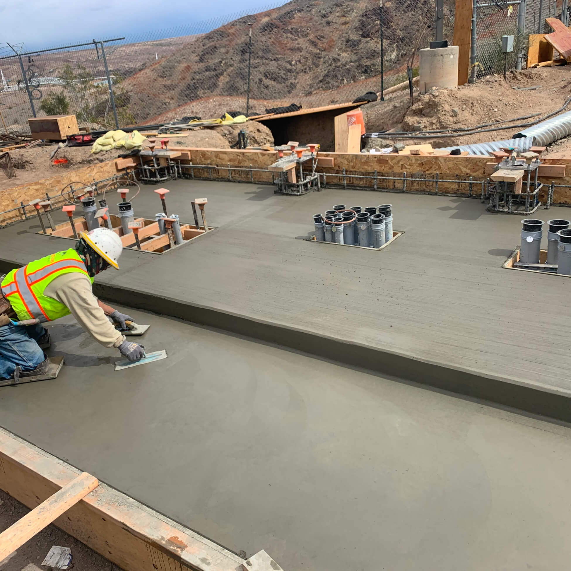 Construction worker smoothing freshly poured concrete foundation with finishing tools at a building site.