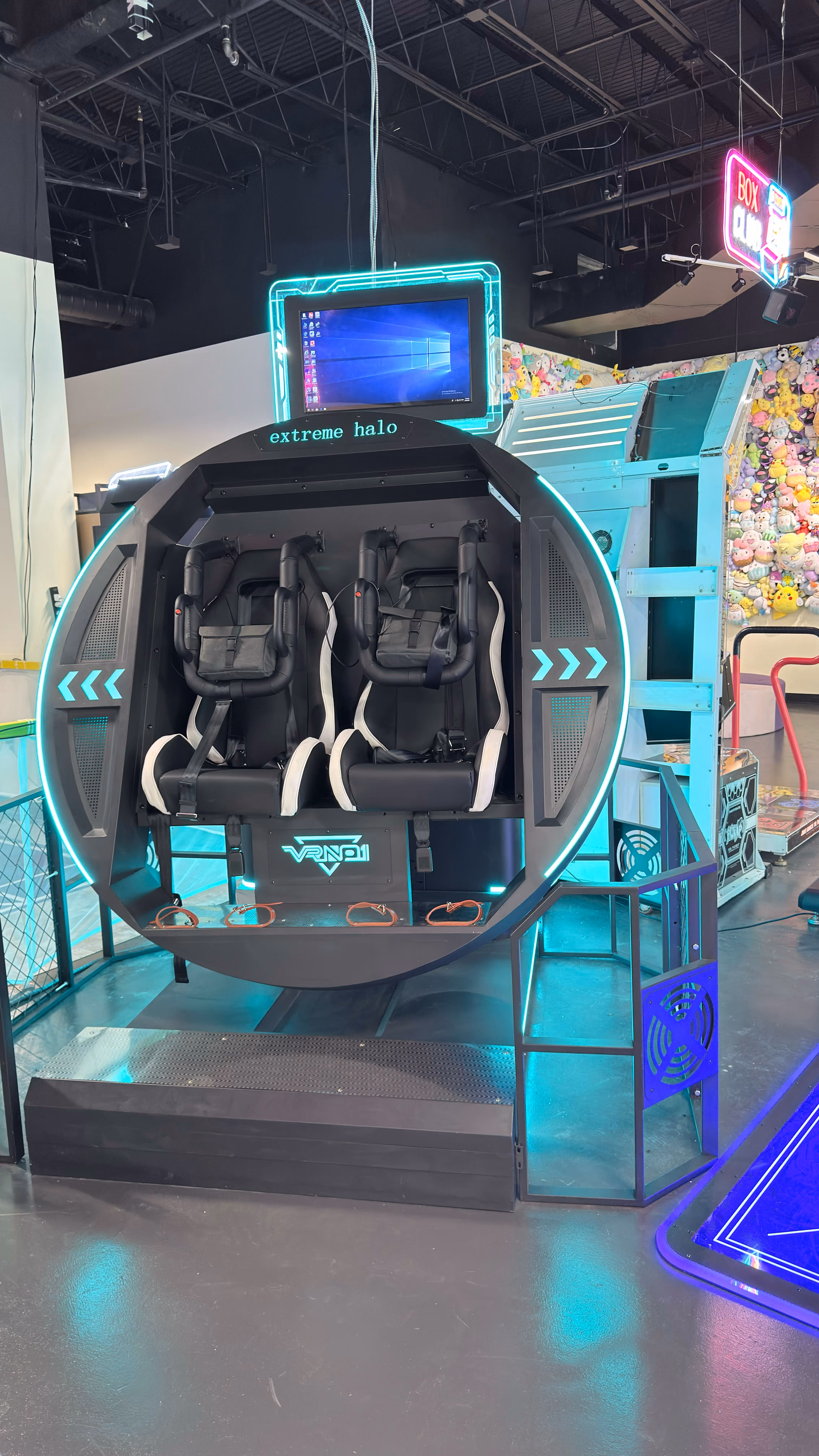 Virtual reality ride machine named 'extreme halo' with two black and white seats and a screen above in an arcade.