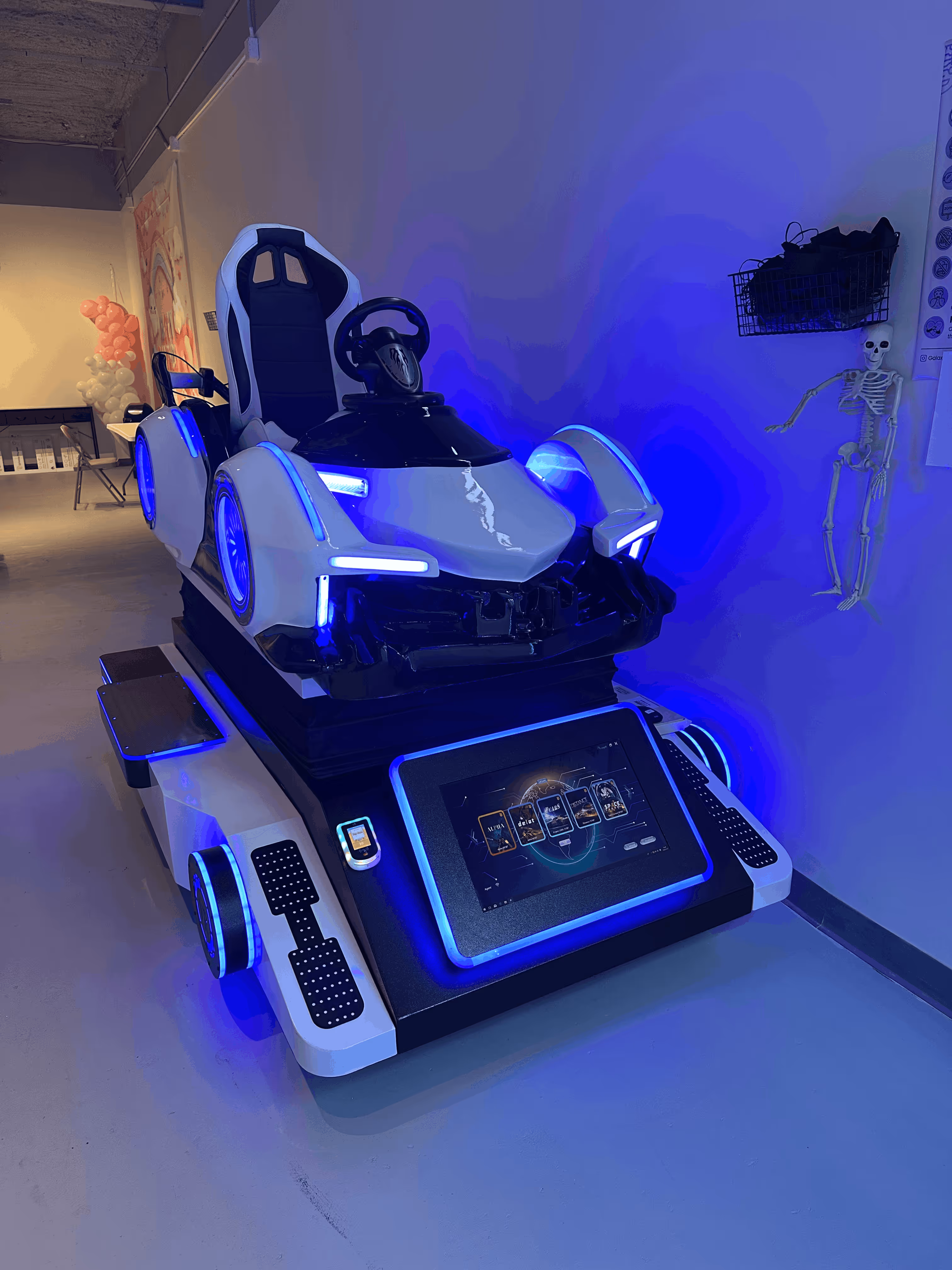 White and black arcade racing simulator chair with blue LED lights and large touchscreen control panel.