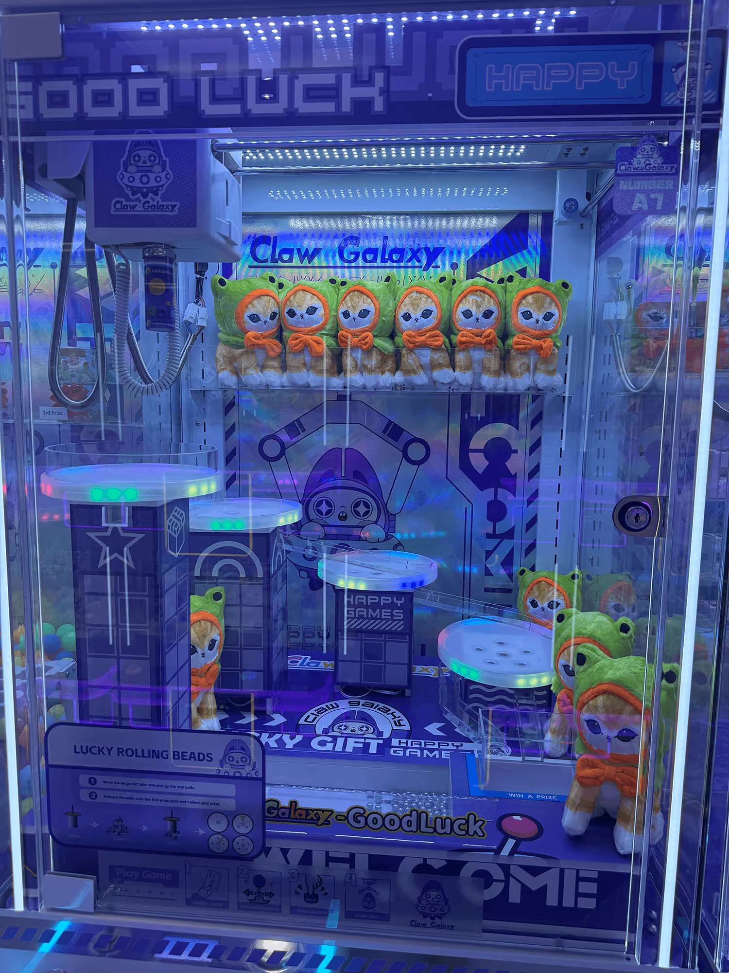 Claw Galaxy arcade claw machine with plush toys dressed as frogs wearing green hoods and orange bow ties inside.