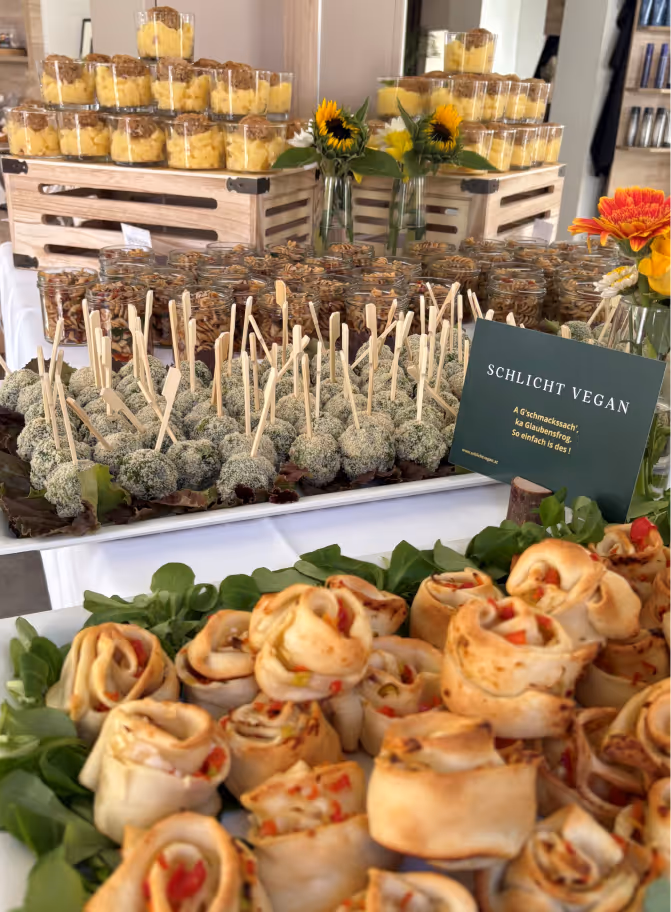 Verschiedene vegane Fingerfood-Variationen auf einem Buffet mit Sonnenblumen und einem Schild 'Schlicht Vegan'.