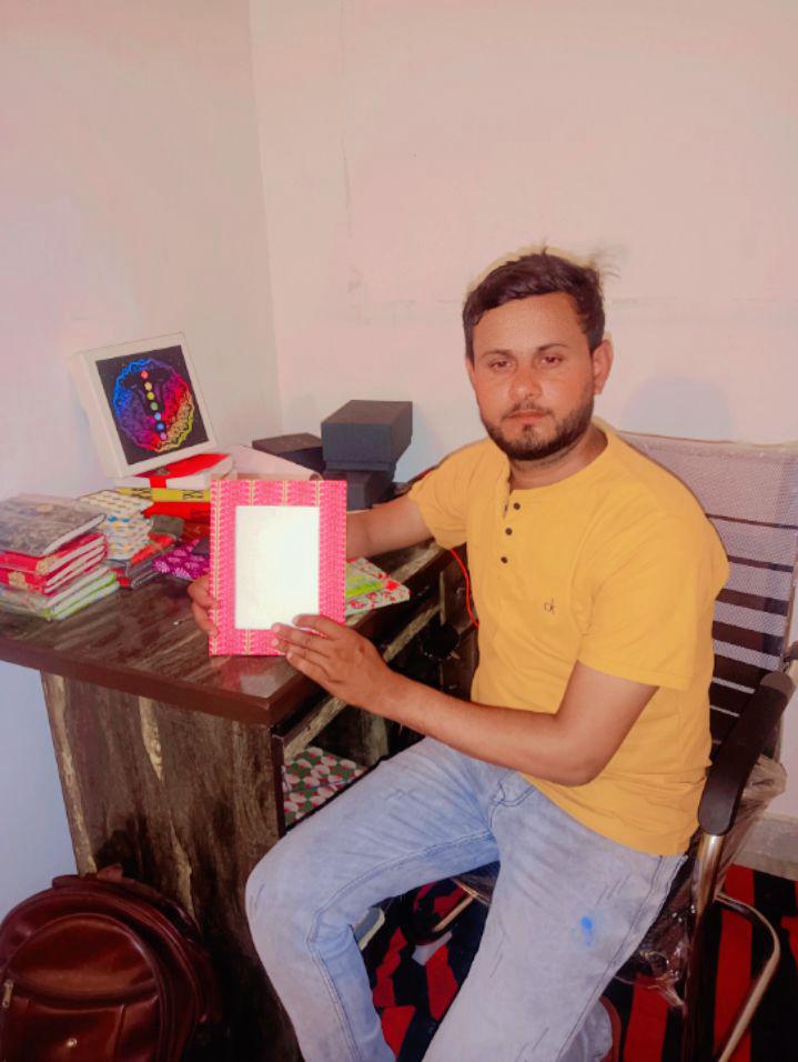Man in a yellow shirt sitting at a desk holding a red patterned notebook with a blank white cover.