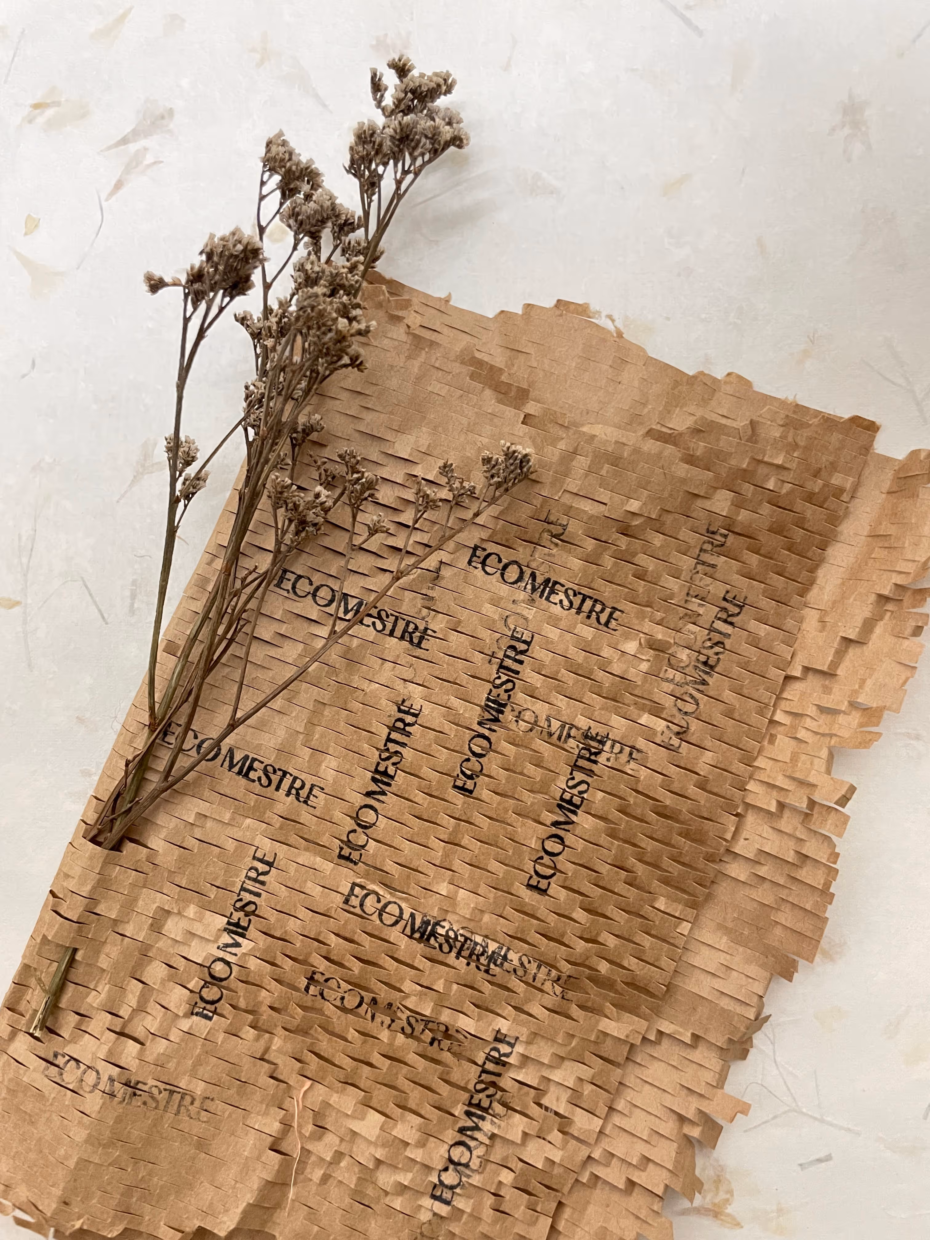 Dried flowers wrapped in brown perforated paper printed with the word ECOMESTRE multiple times.