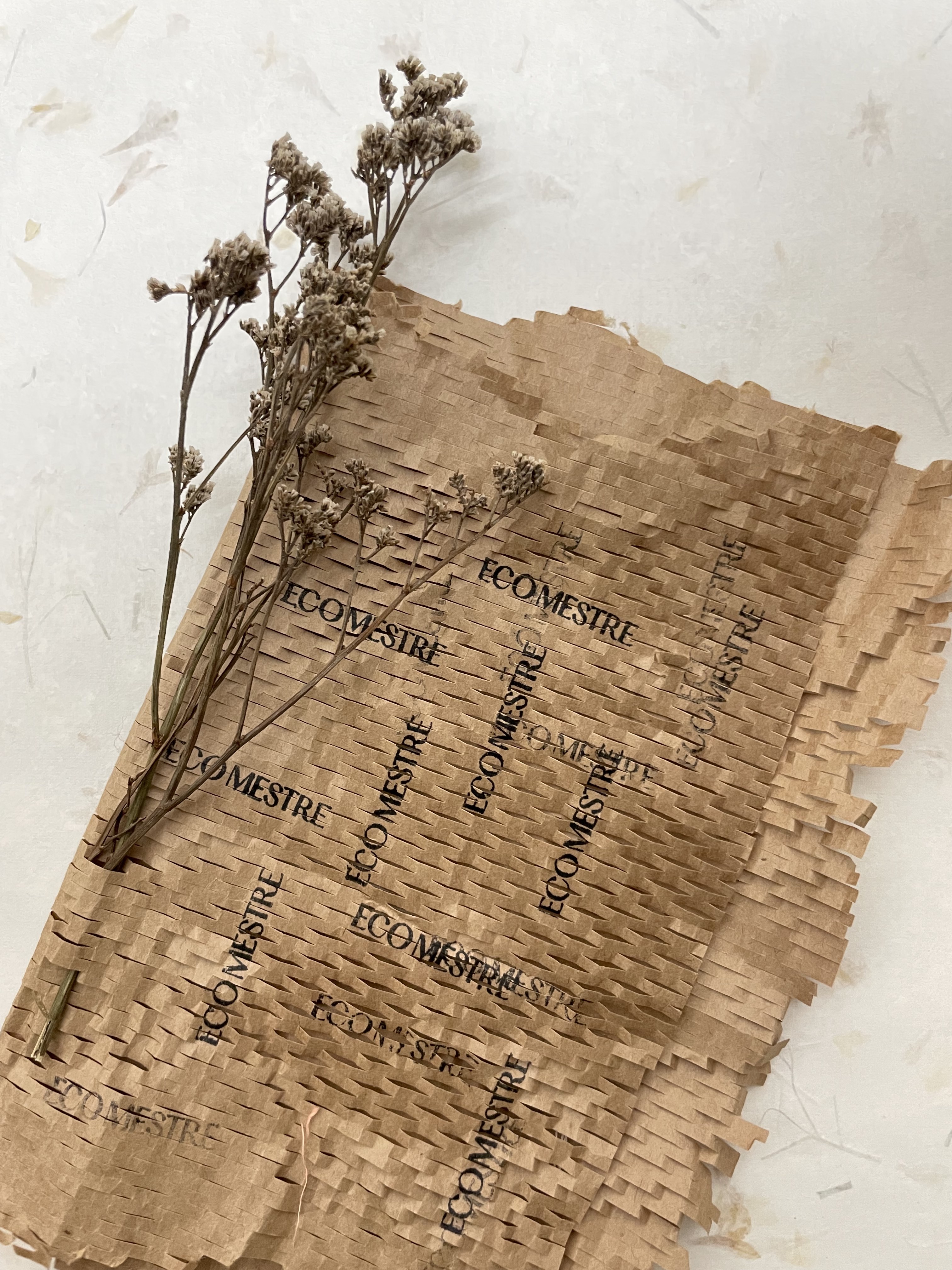 Dried flowers wrapped in brown perforated paper printed with the word ECOMESTRE multiple times.