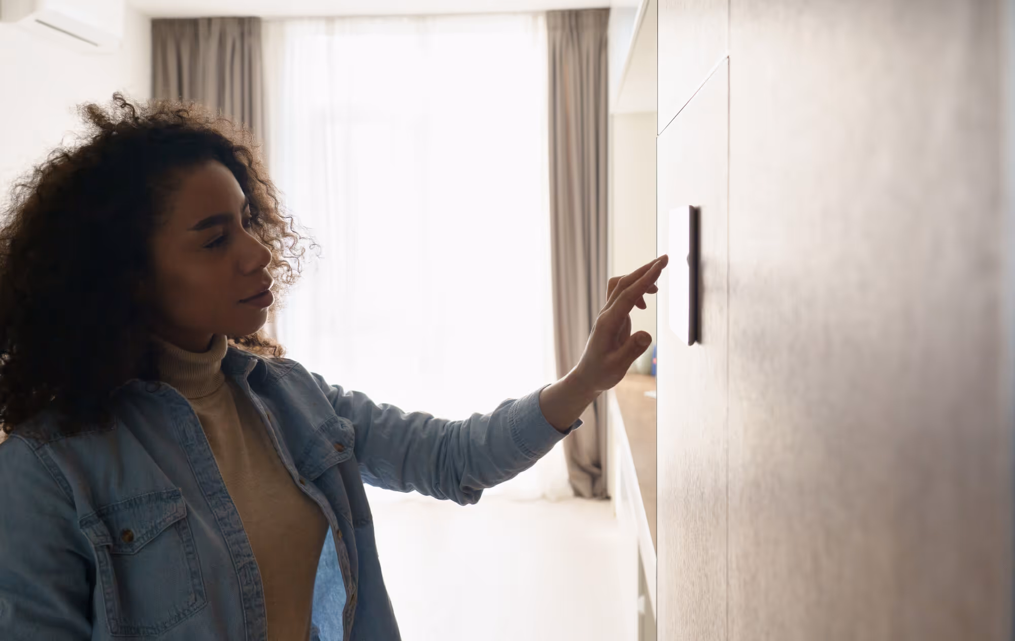 Woman with curly hair touching wall switch in bright room