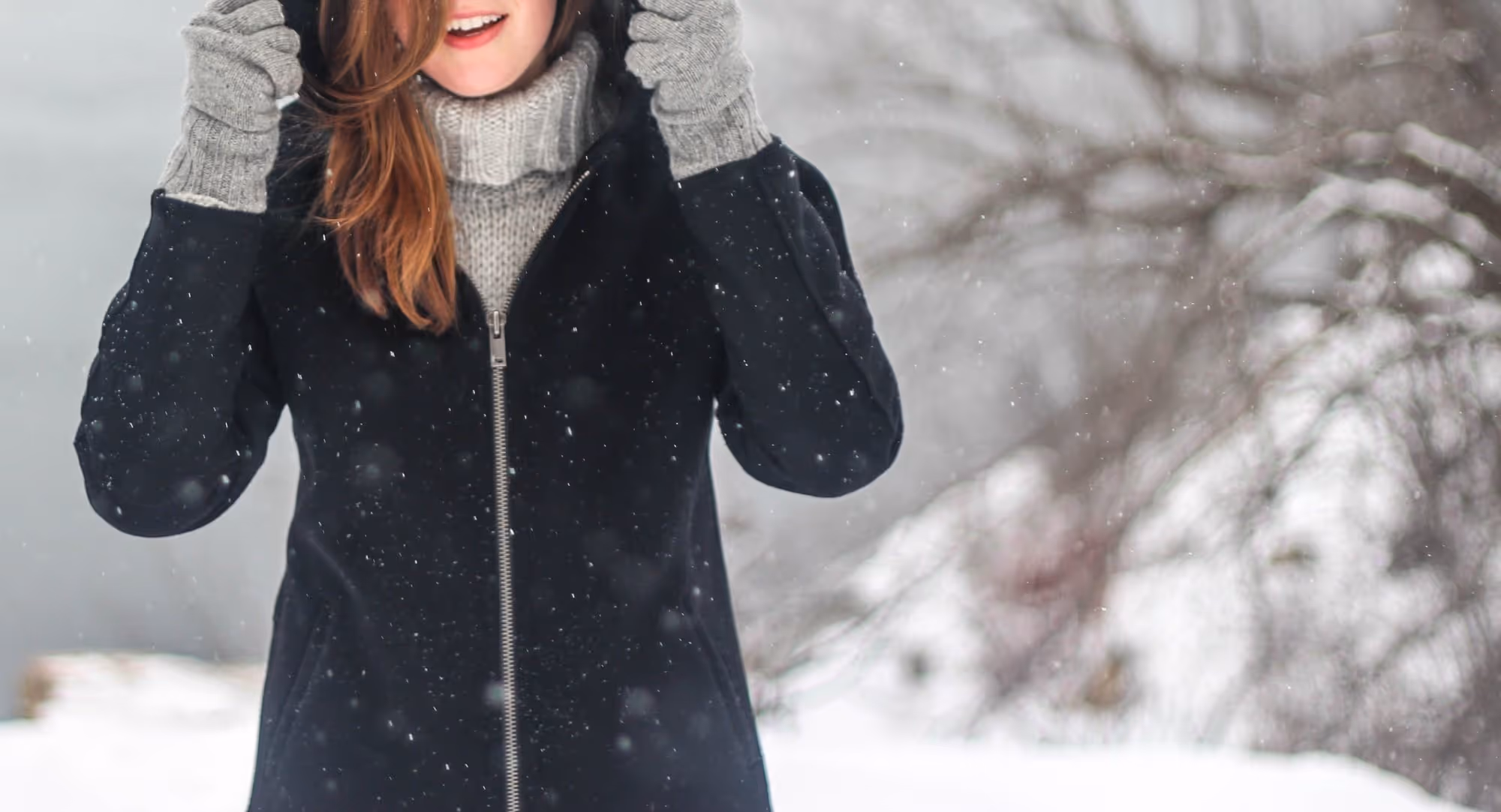 Smiling person in winter coat and gloves enjoying snowfall