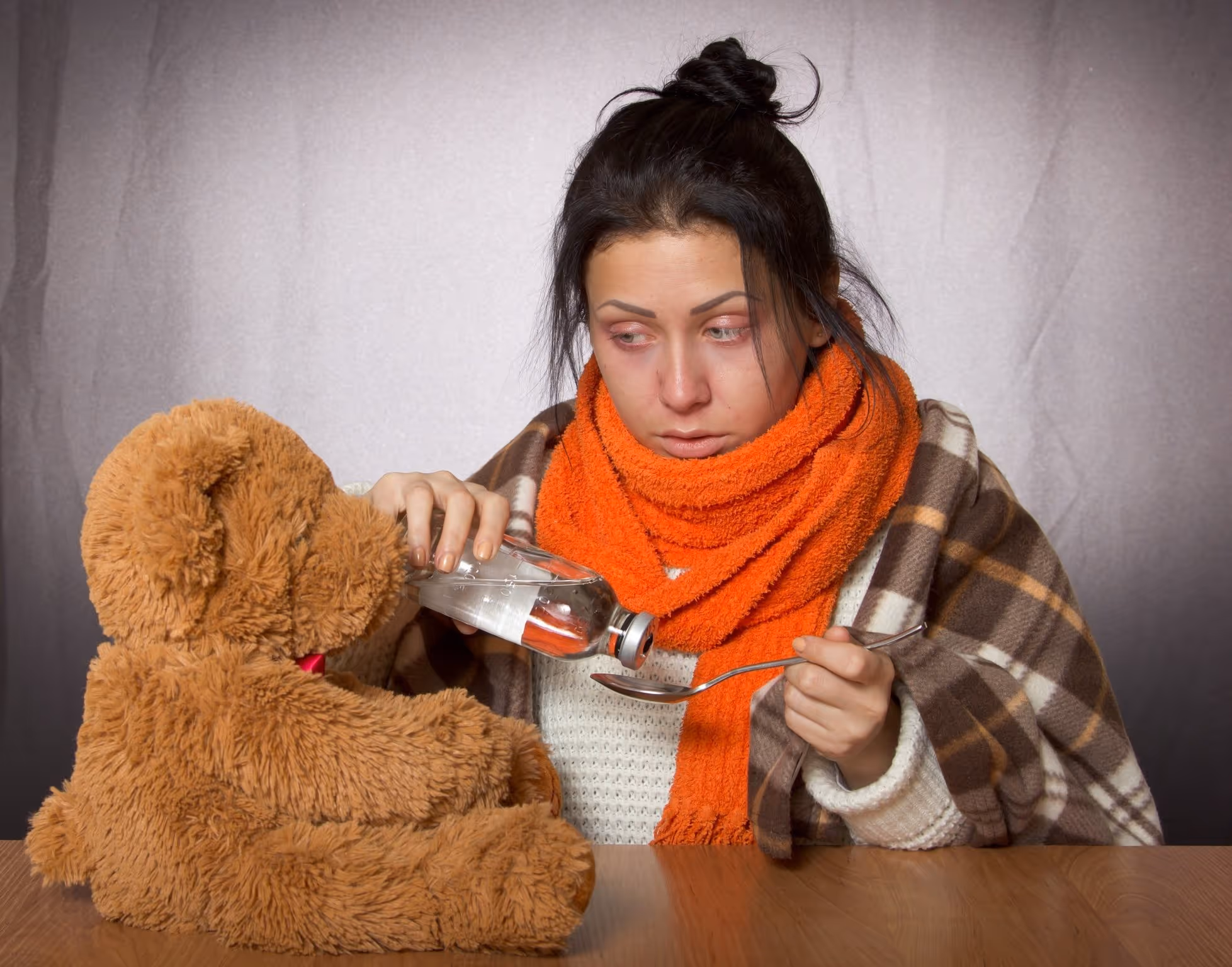 Sick person in orange scarf giving medicine to teddy bear