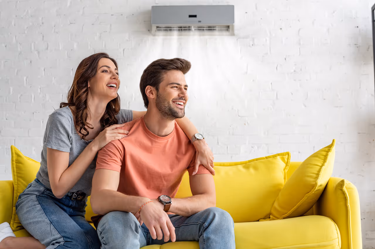 Couple laughing together on yellow couch with air conditioner in background