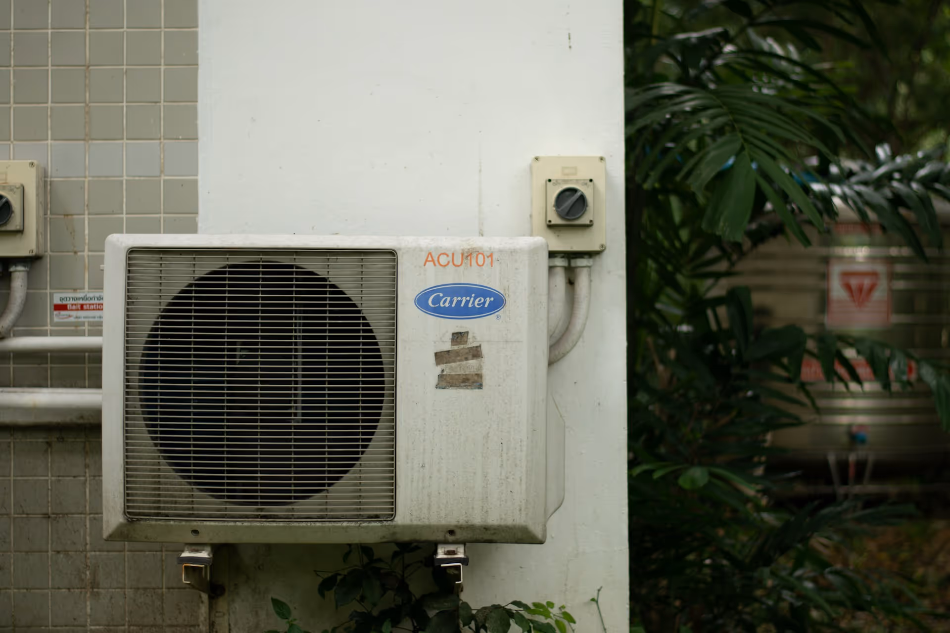 Carrier air conditioning unit mounted on tiled wall near green foliage
