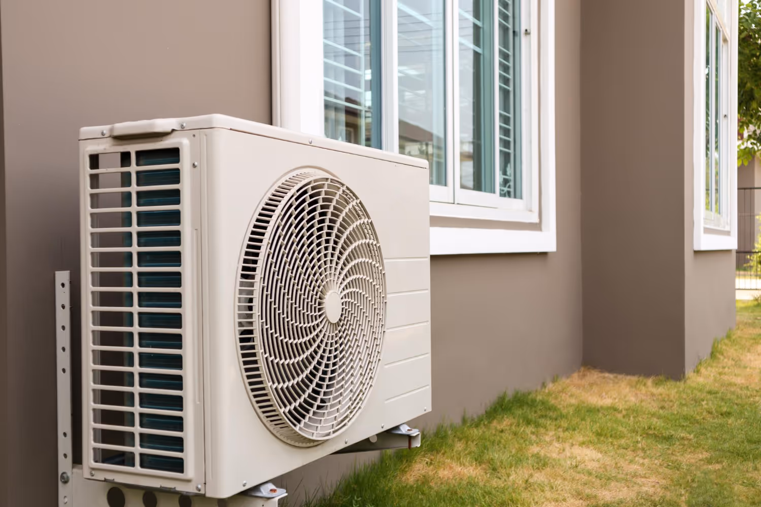 White air conditioning unit mounted on wall near windows and grass