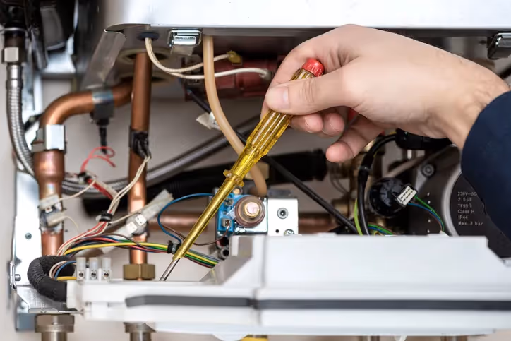 Close-up of technician's hand using screwdriver on boiler components with wires and pipes