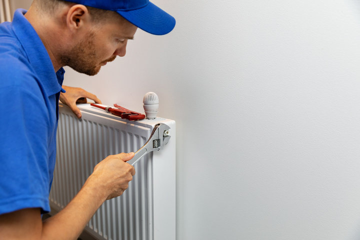 Technician in blue fixing radiator with wrench and adjusting valve