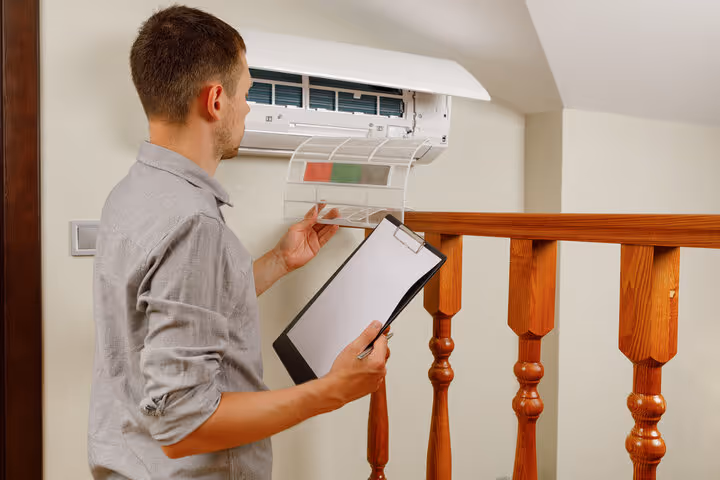 Technician checking air conditioning unit with clipboard near wooden railing