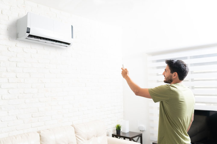 Person adjusting wall-mounted air conditioner in minimalist living room