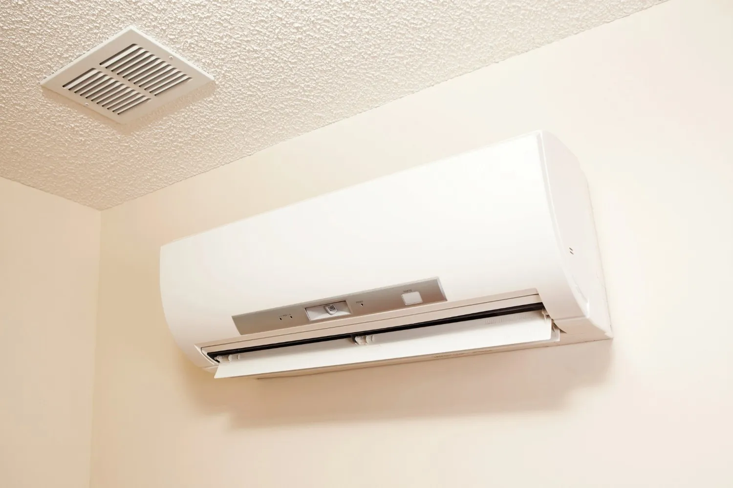 White wall-mounted air conditioning unit with vent near ceiling